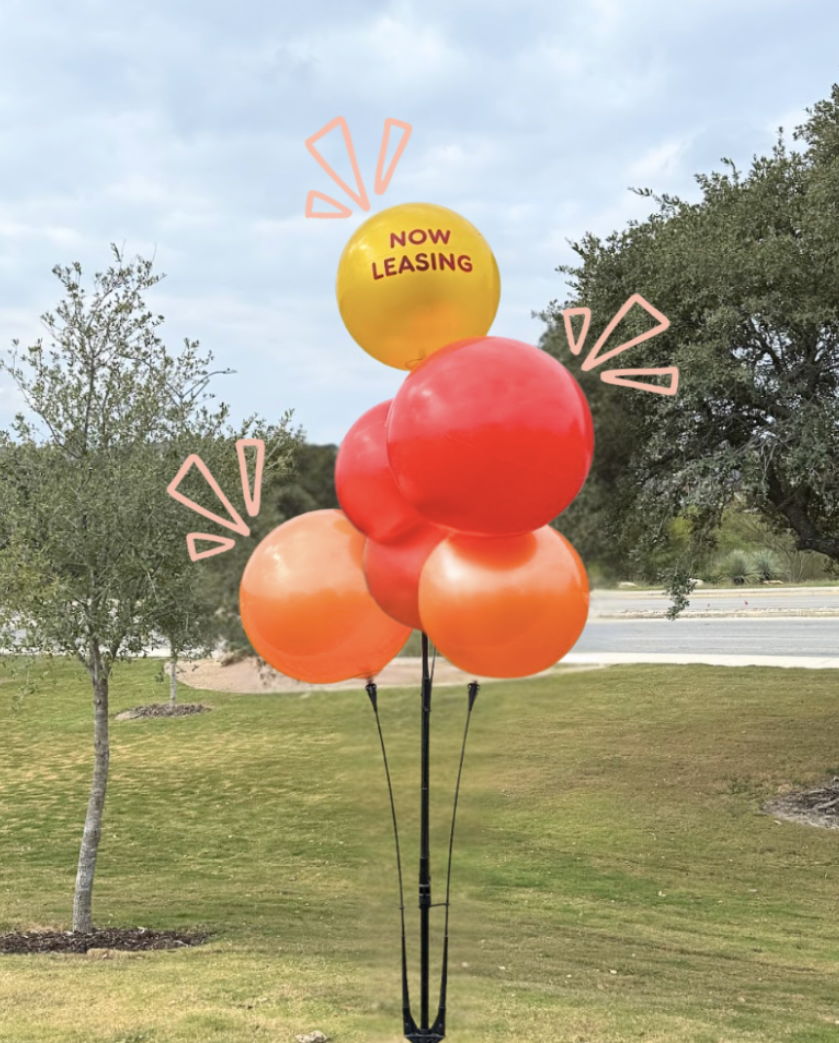 Cluster of red, orange, and yellow balloons outdoors, with the top balloon reading &ldquo;Now Leasing.&rdquo;